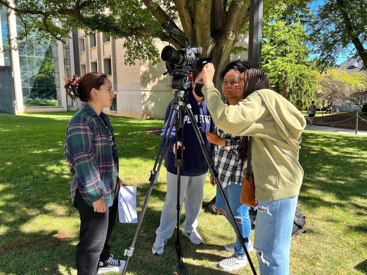 Four students gather around a video camera on a sunny day