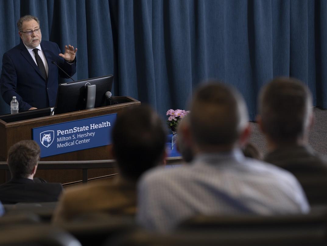 Dr. David Goldenberg stands at a lectern speaking to an audience.