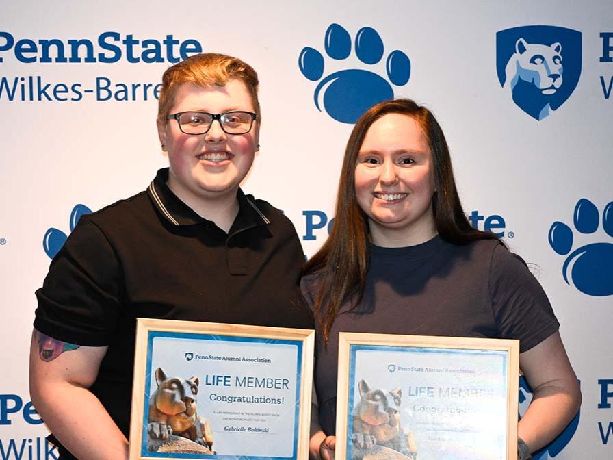 Two students standing with awards against a wall with Penn State Wilkes-Barre logos