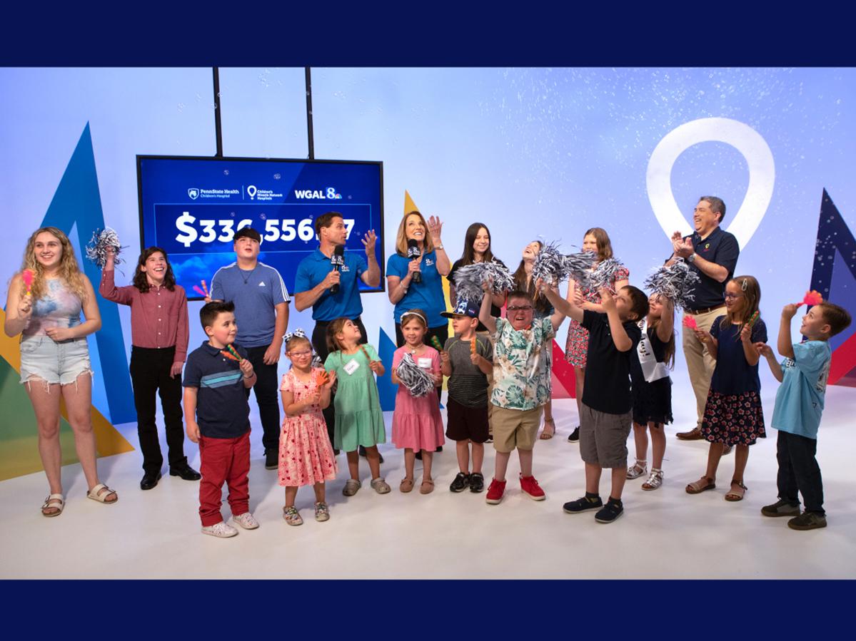 A group of adults and children join together in applause as they stand in a TV studio.