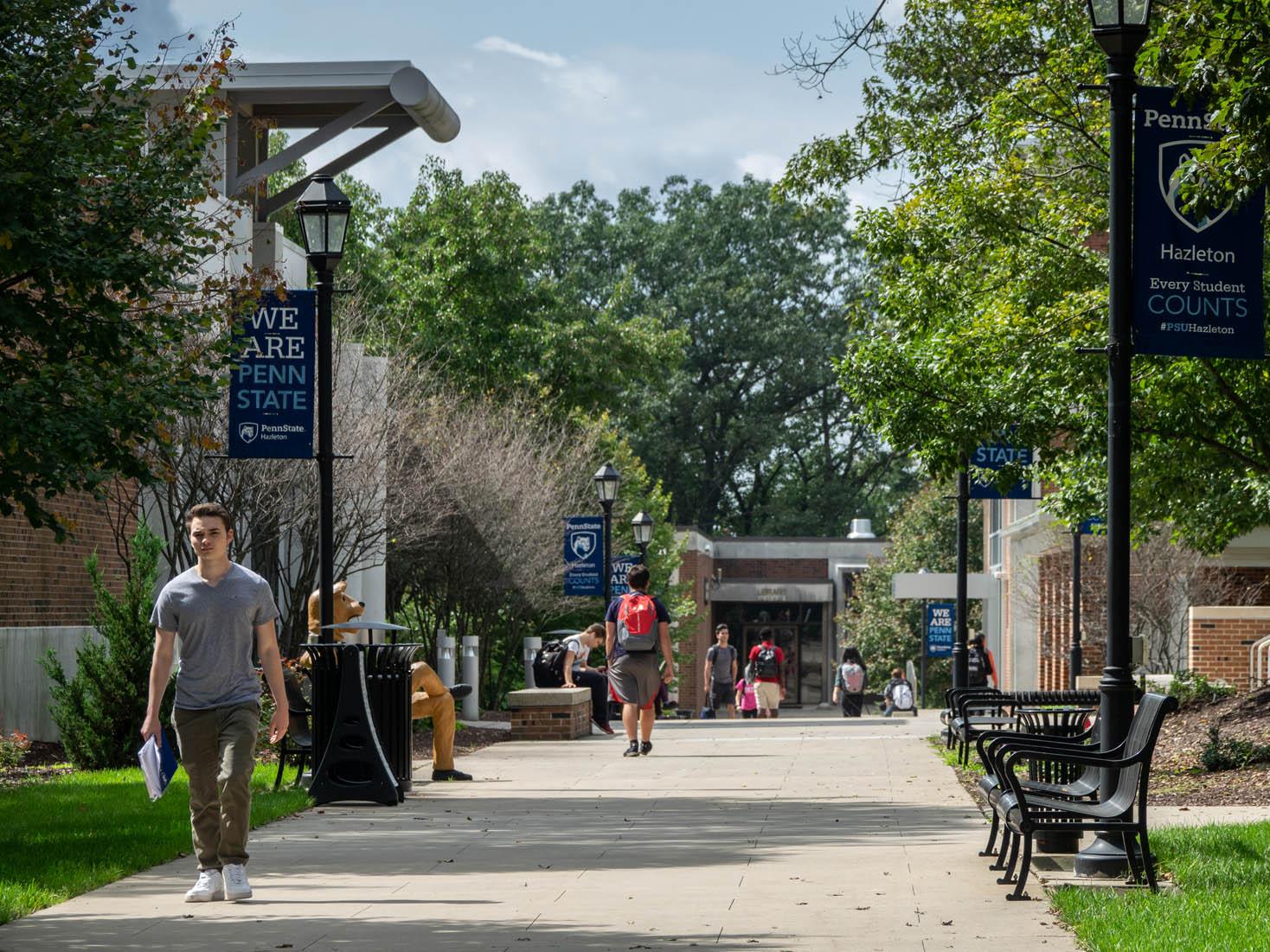 Students walking on a sidewalk at a college campus on a sunny day.