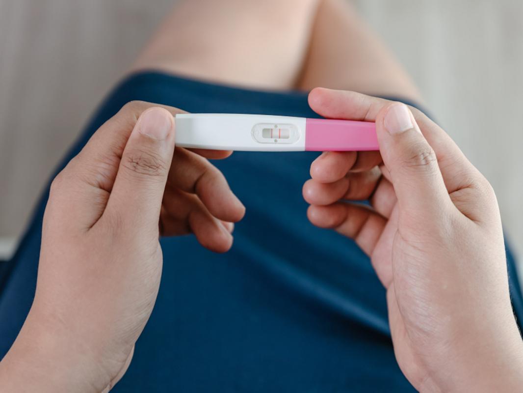 Close-up of a woman’s hands holding a pregnancy test kit and waiting for positive result in her bedroom.