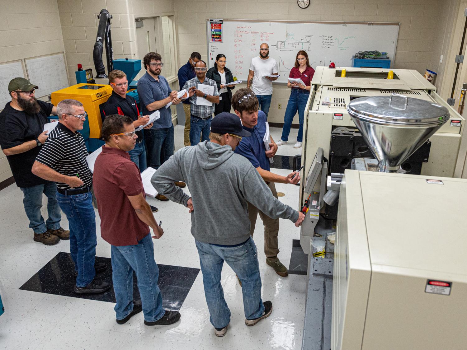 A group of people stand around equipment during a workshop taught by an instructor.
