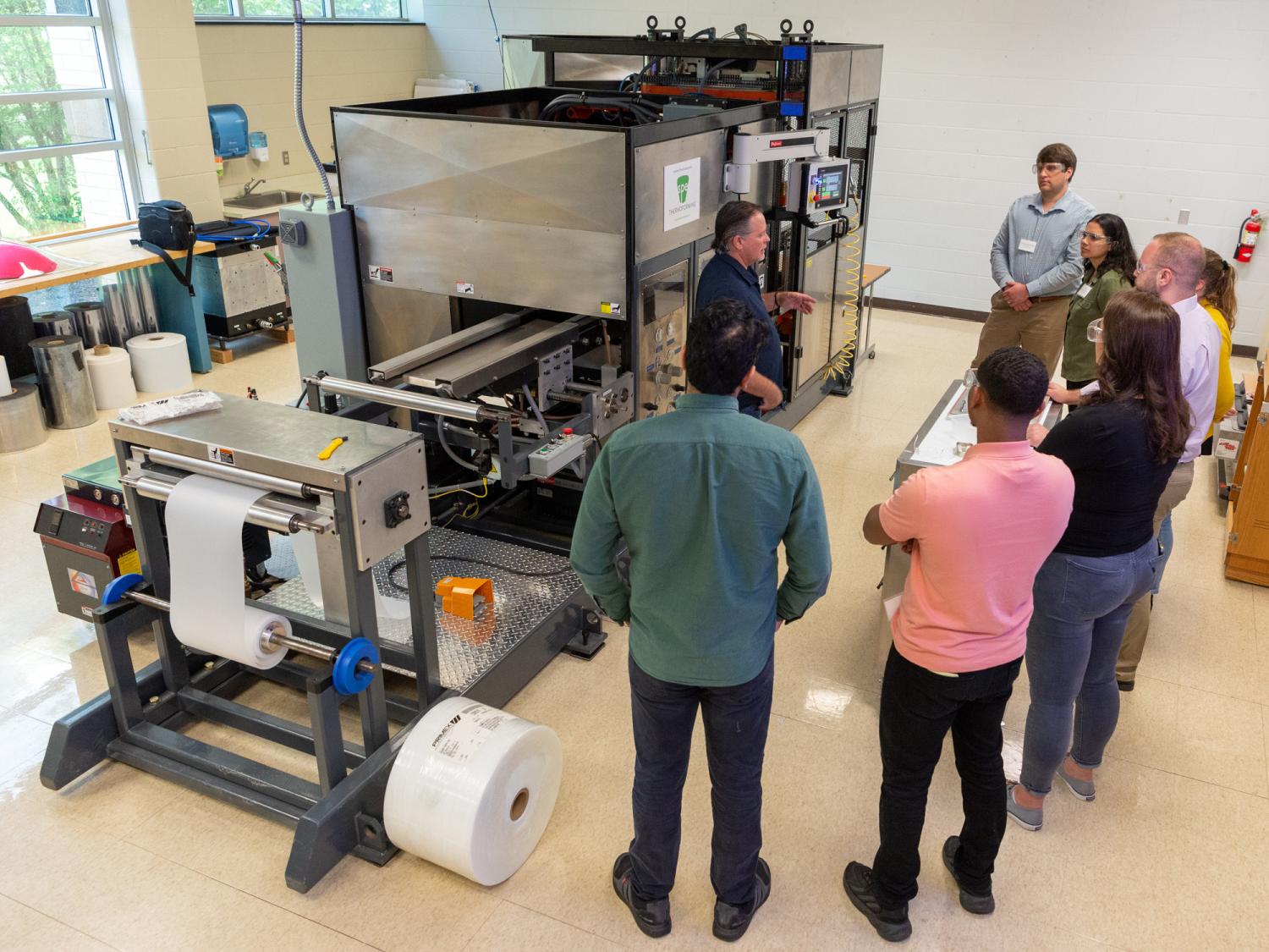 Several people stand around a piece of equipment listening to a workshop teacher.