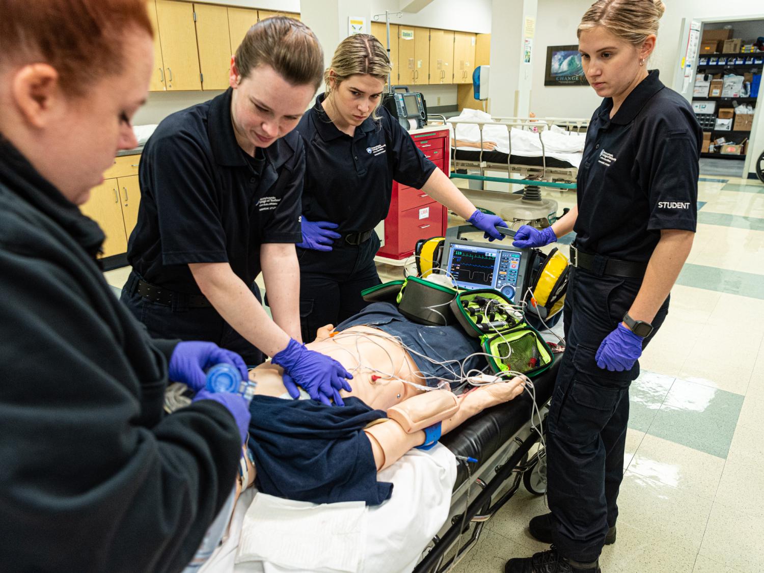 Several people stand around a medical manikin on a table