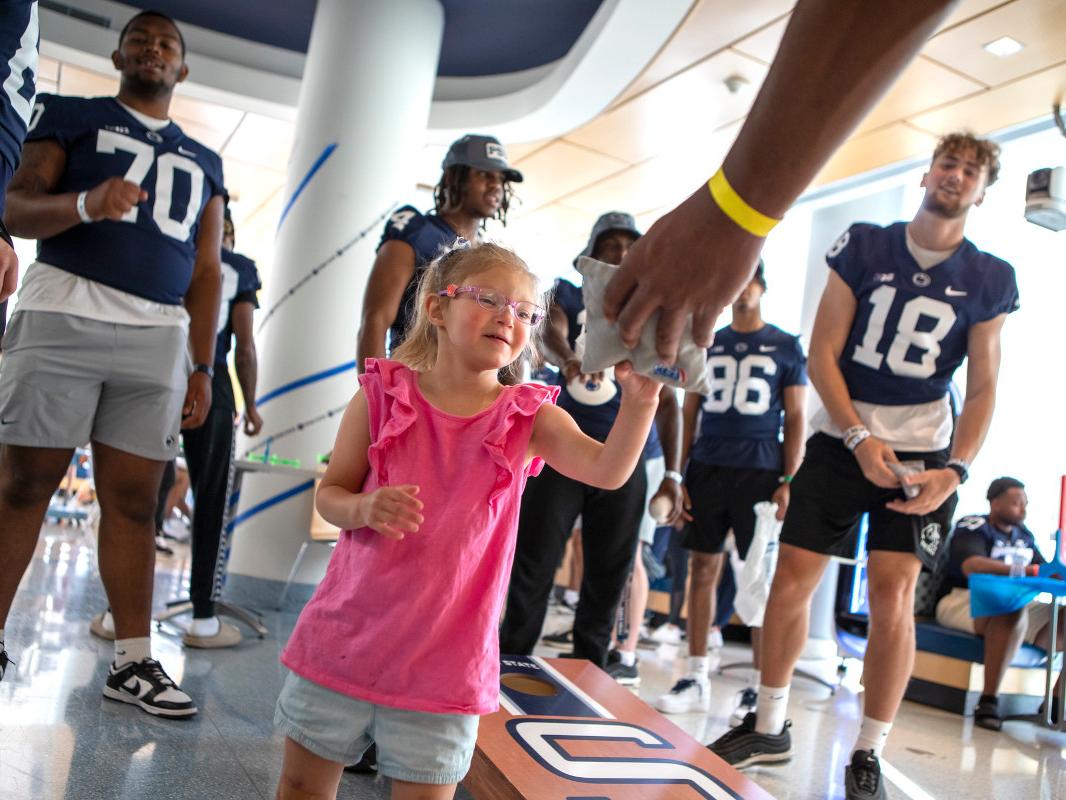 A young girl plays a bean bag game with members of the Penn State Football Team