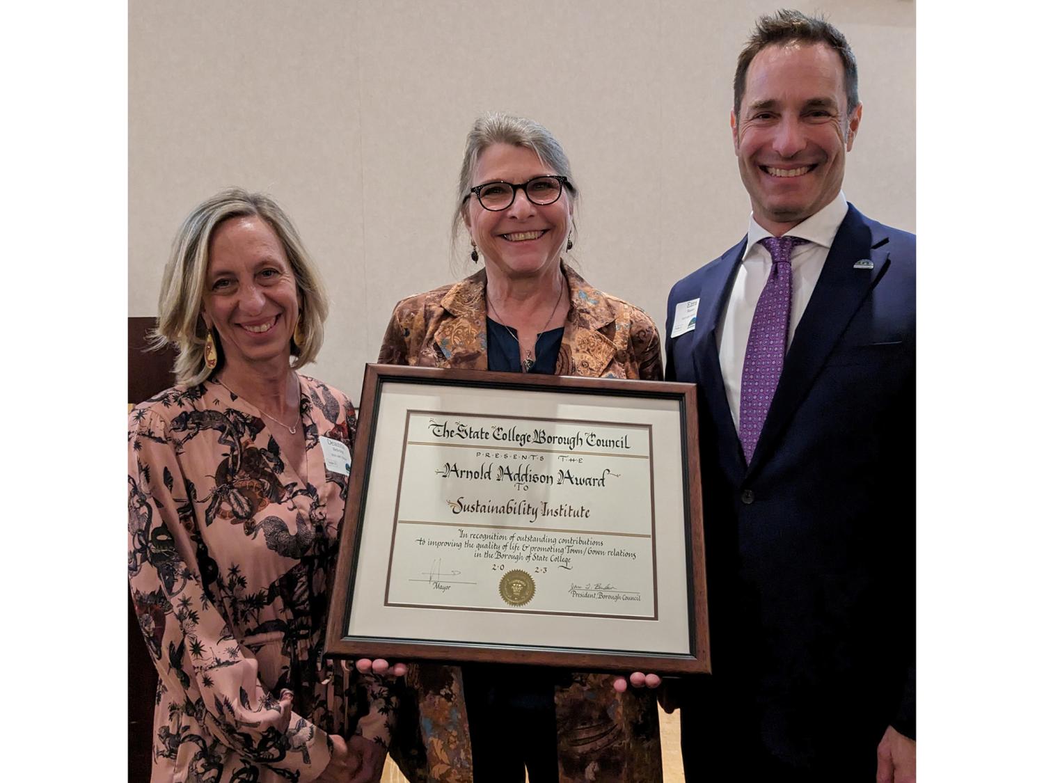 two women standing with a man accepting an award in a picture frame