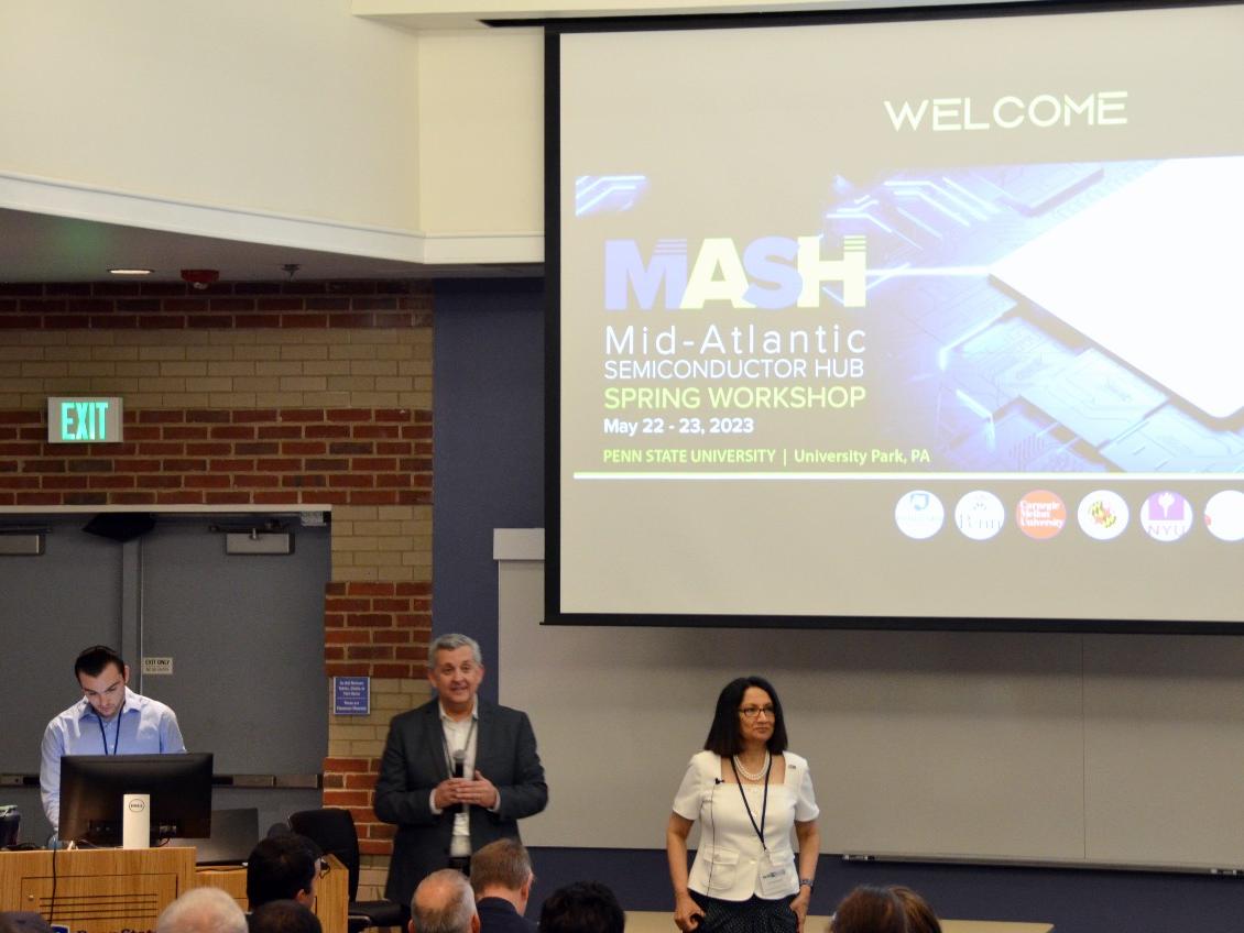 Three people in front of a group of people with a large screen.