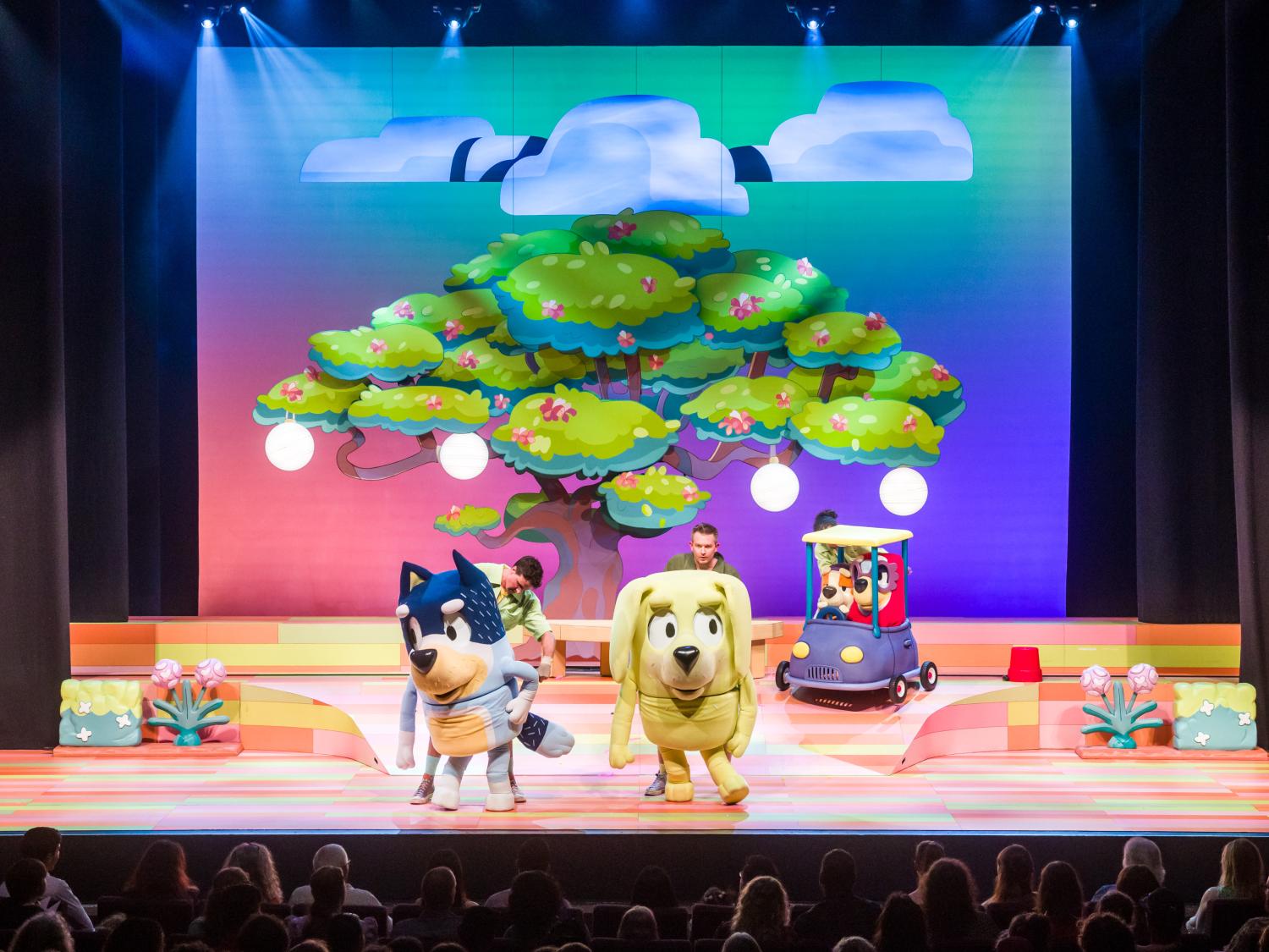 Two oversized cartoonish dog puppets are shown standing center stage.