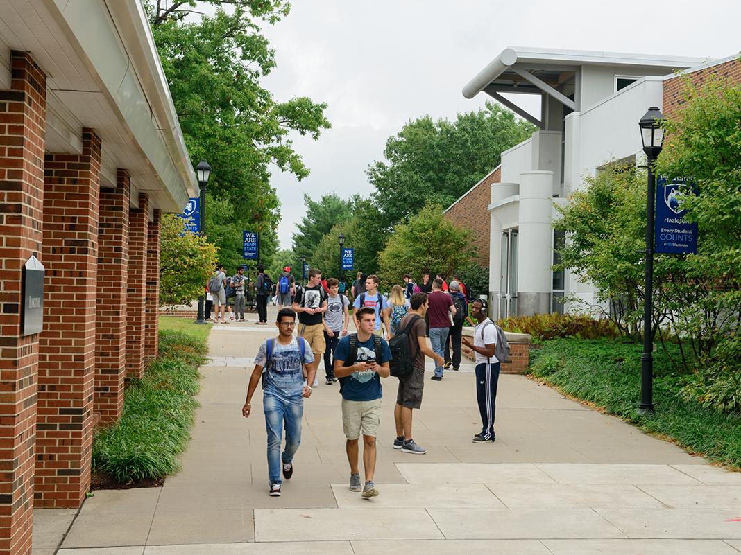 Crowd of students walking along a sidewalk on a college campus.