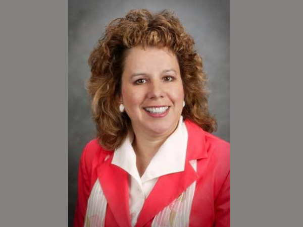 Woman with long, curly light brown hair in a pink blazer with white collared shirt underneath.