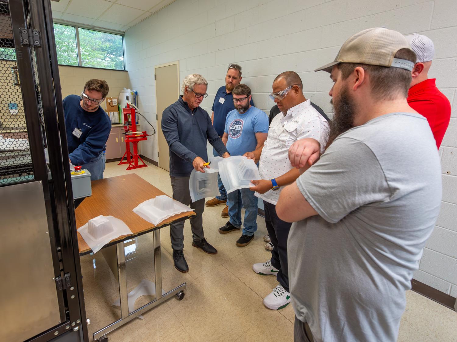 A group of people watch some thermoforming equipment in action.
