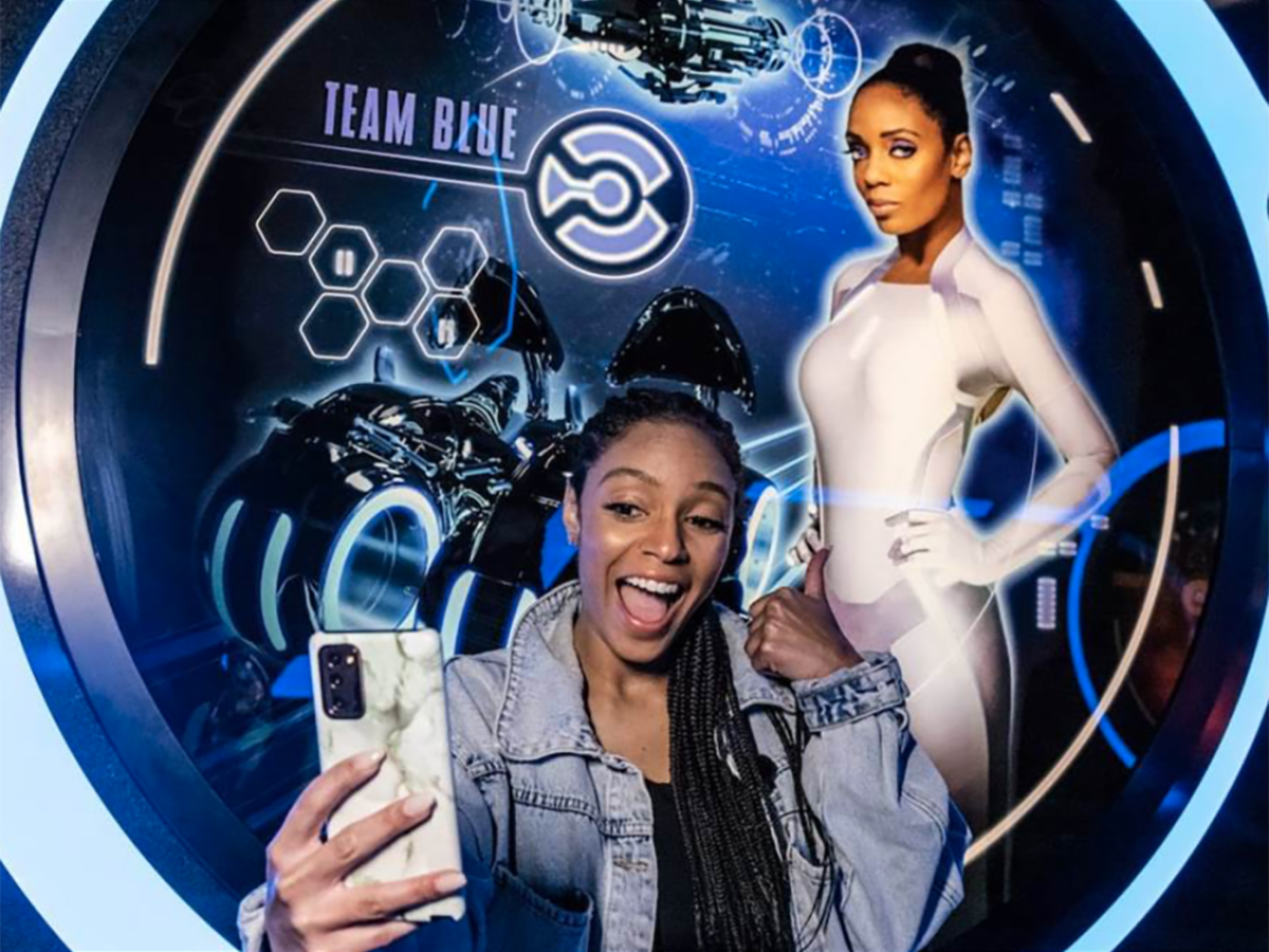 A photo of Faren Collins taking a selfie with an image of herself and the Tron ride at Disney