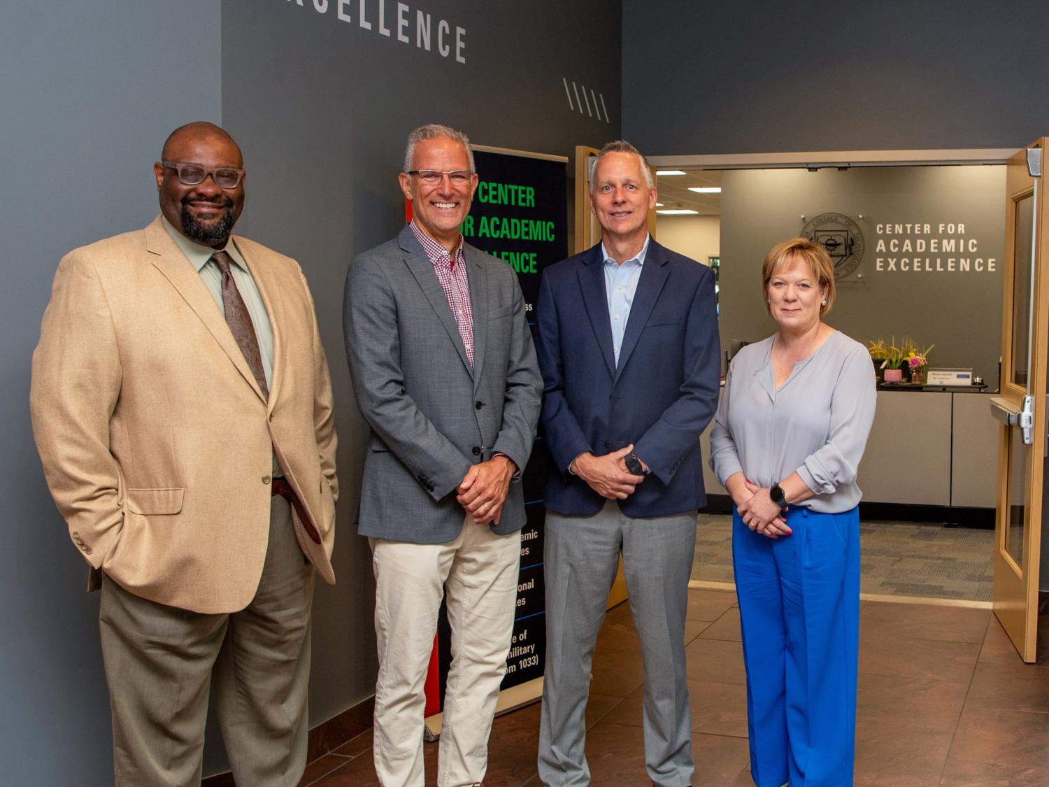 Four people stand shoulder to shoulder in Penn College's Center for Academic Excellence