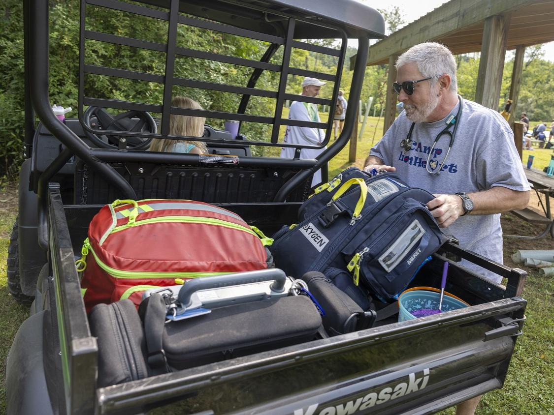 A man places packs in the back of a utility vehicle. He wears a Camp Lionheart T-shirt.