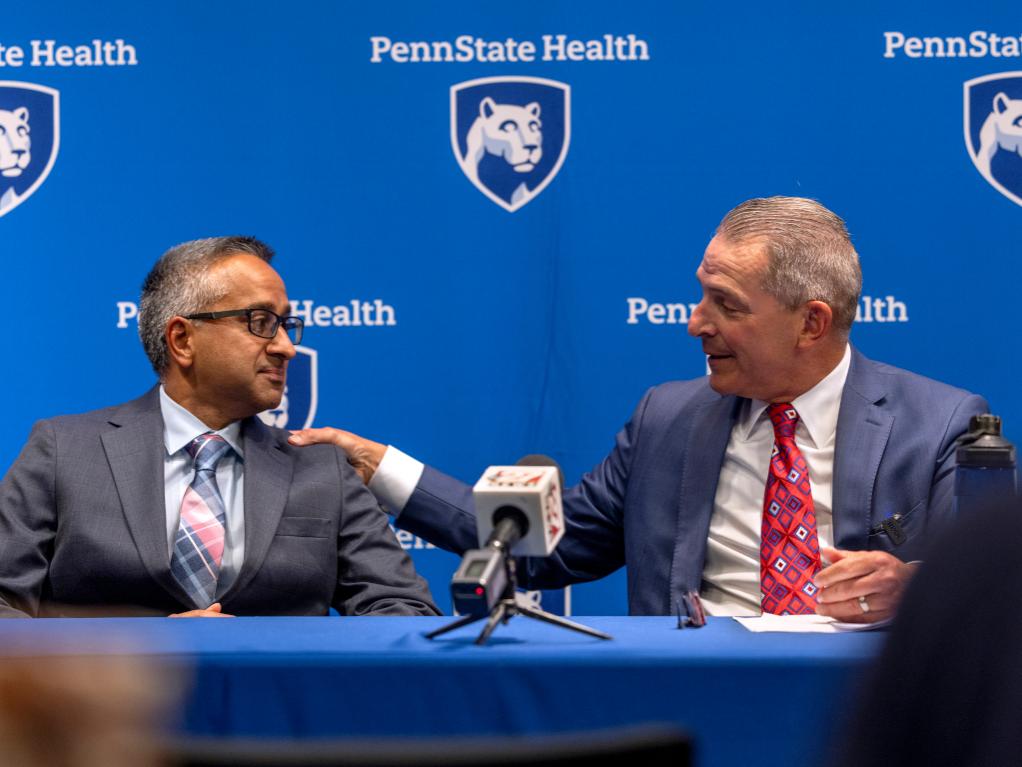 Two men in suits sit next to each other, talking and smiling.