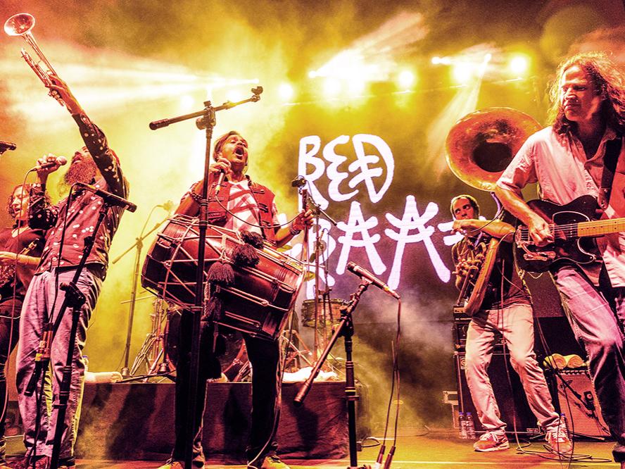 A group of diverse musicians play brass and percussion instruments on a stage.