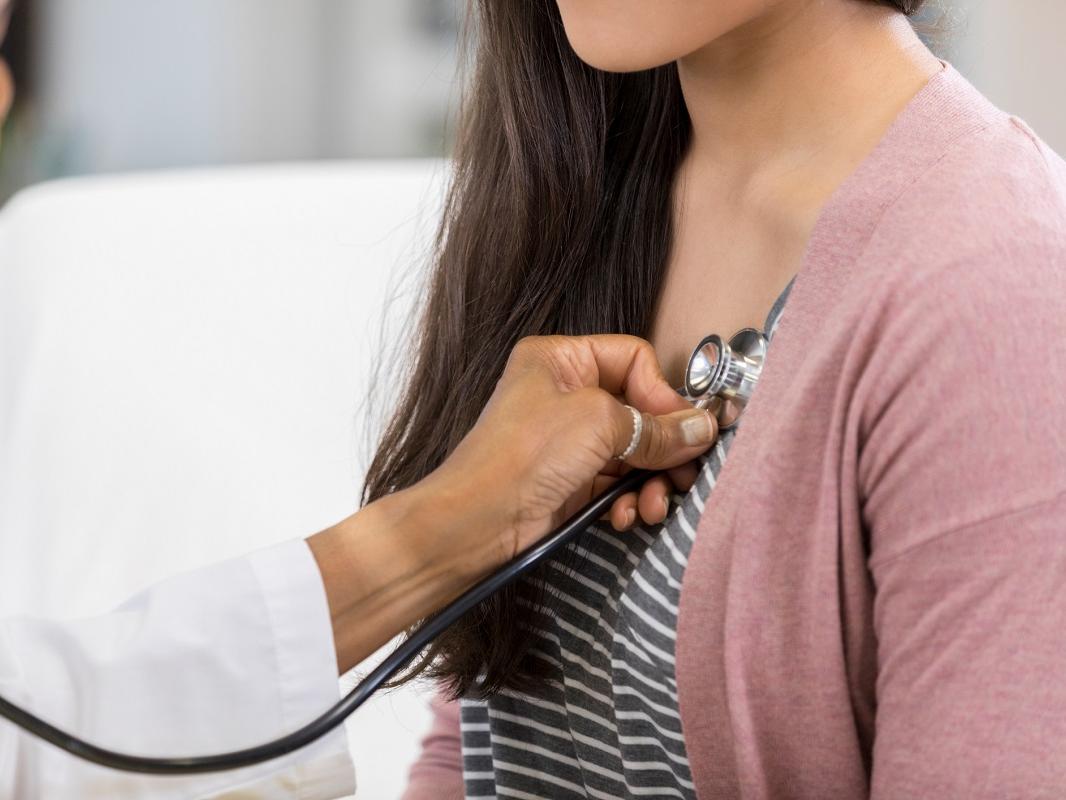 A doctor listens to a young woman’s heartbeat with a stethoscope.