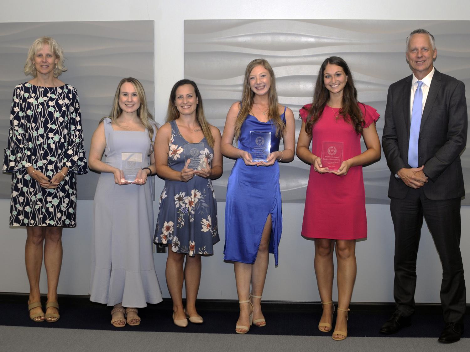 Six people pose for a photo, several of them holding awards.