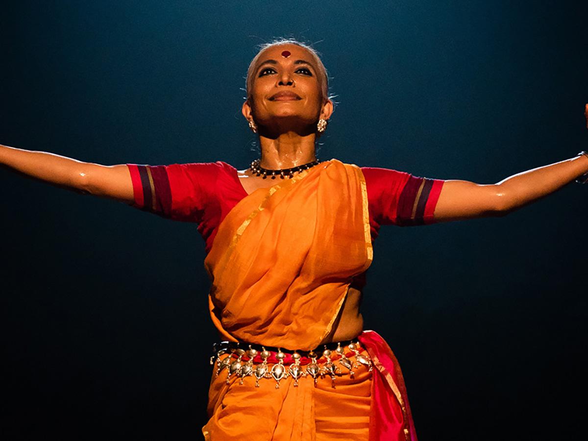 A classical Indian dancer smiles while she stands with her arms outstretched