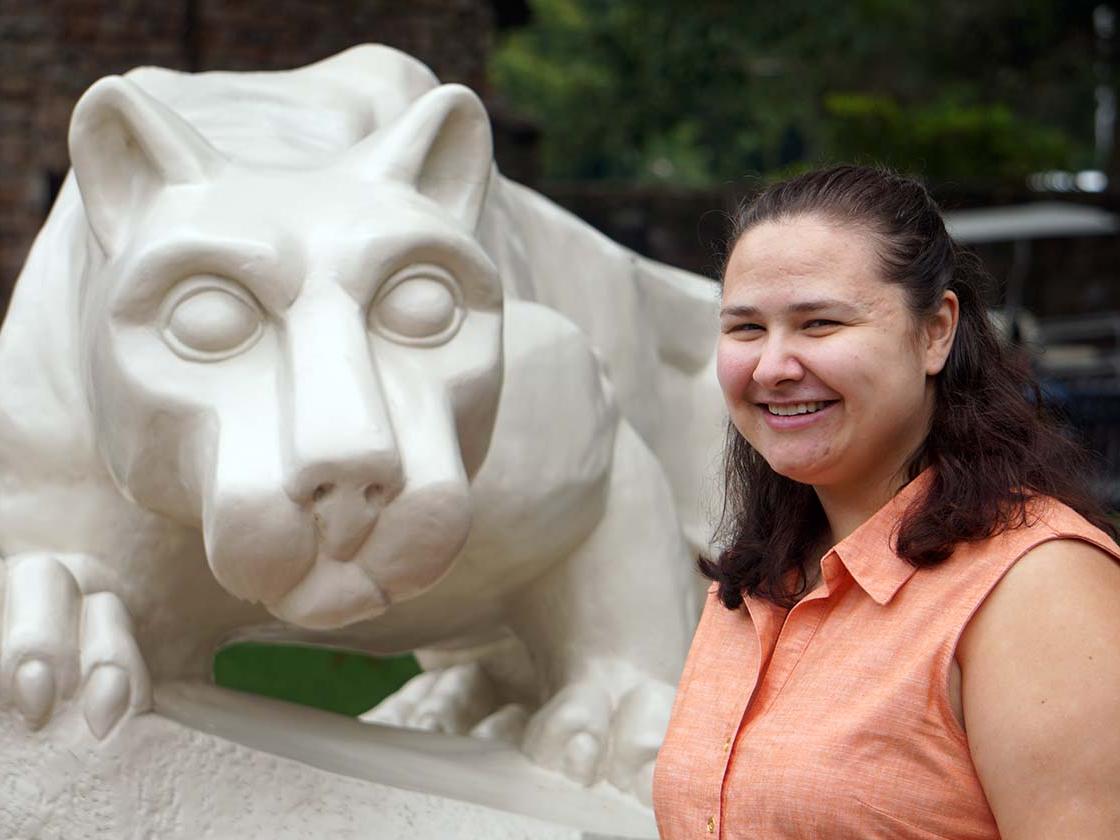 Woman with brown hair and salmon-colored blouse smiling next to stone statue of a lion.