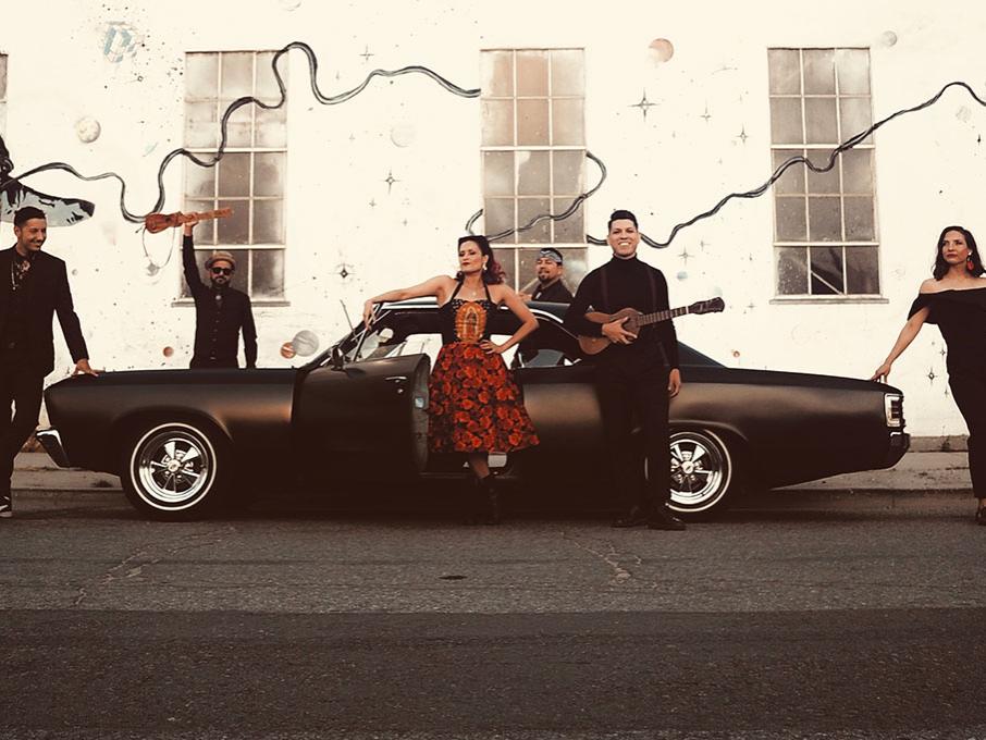 A group of stylishly dressed people stand around a classic hot-rod automobile.