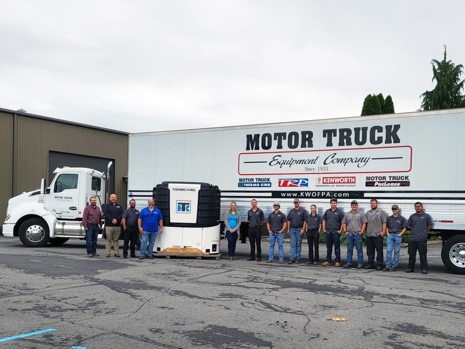 A group of people stand in front of a large trailer refrigeration truck