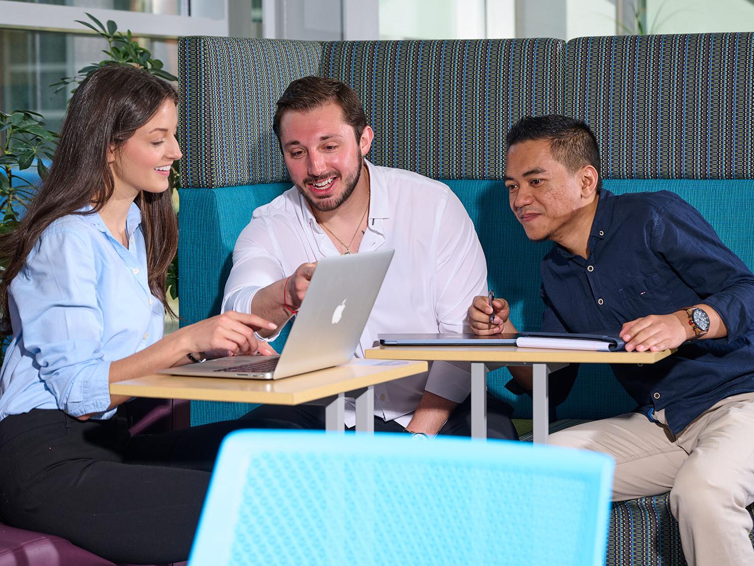 Three students gather around a laptop.