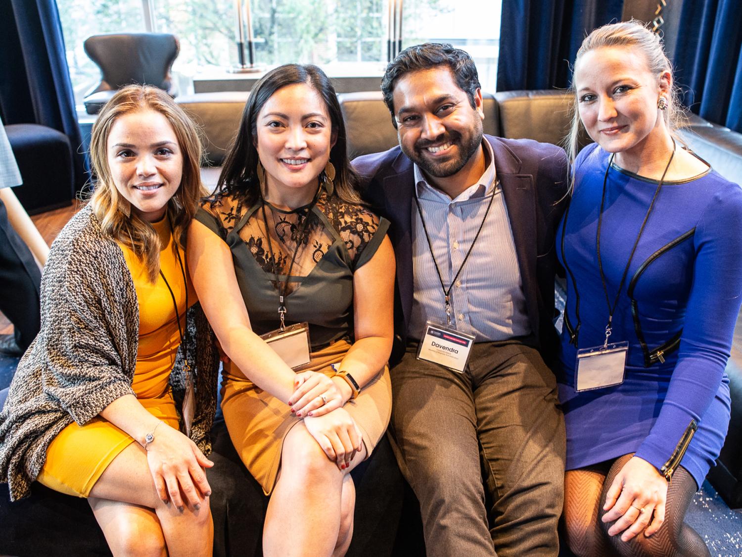 Four people wearing business casual attire sit on a couch and pose for a photo.