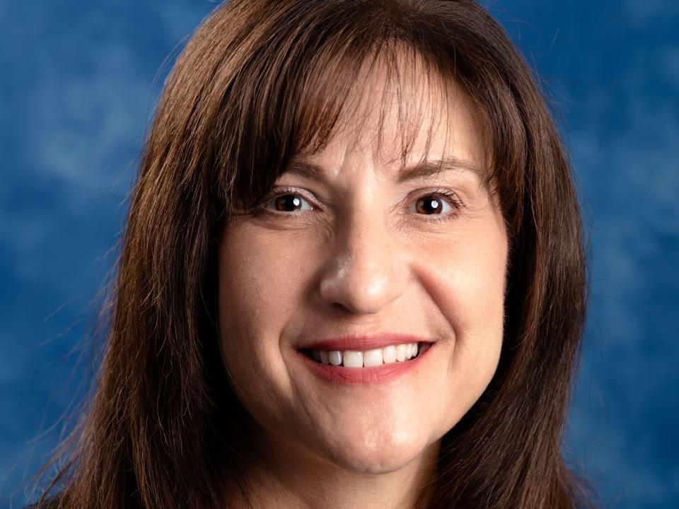 Woman with brown hair wearing a white shirt with black sweater over it.