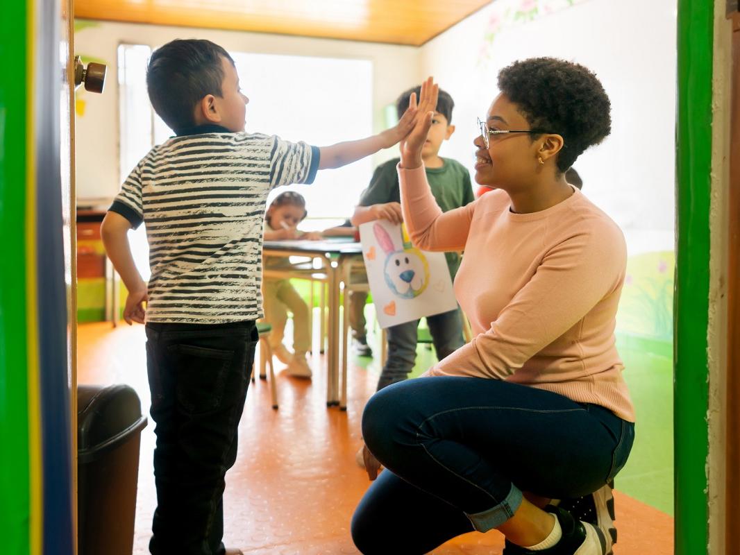 A teacher smiles as she high-fives a student entering the classroom.
