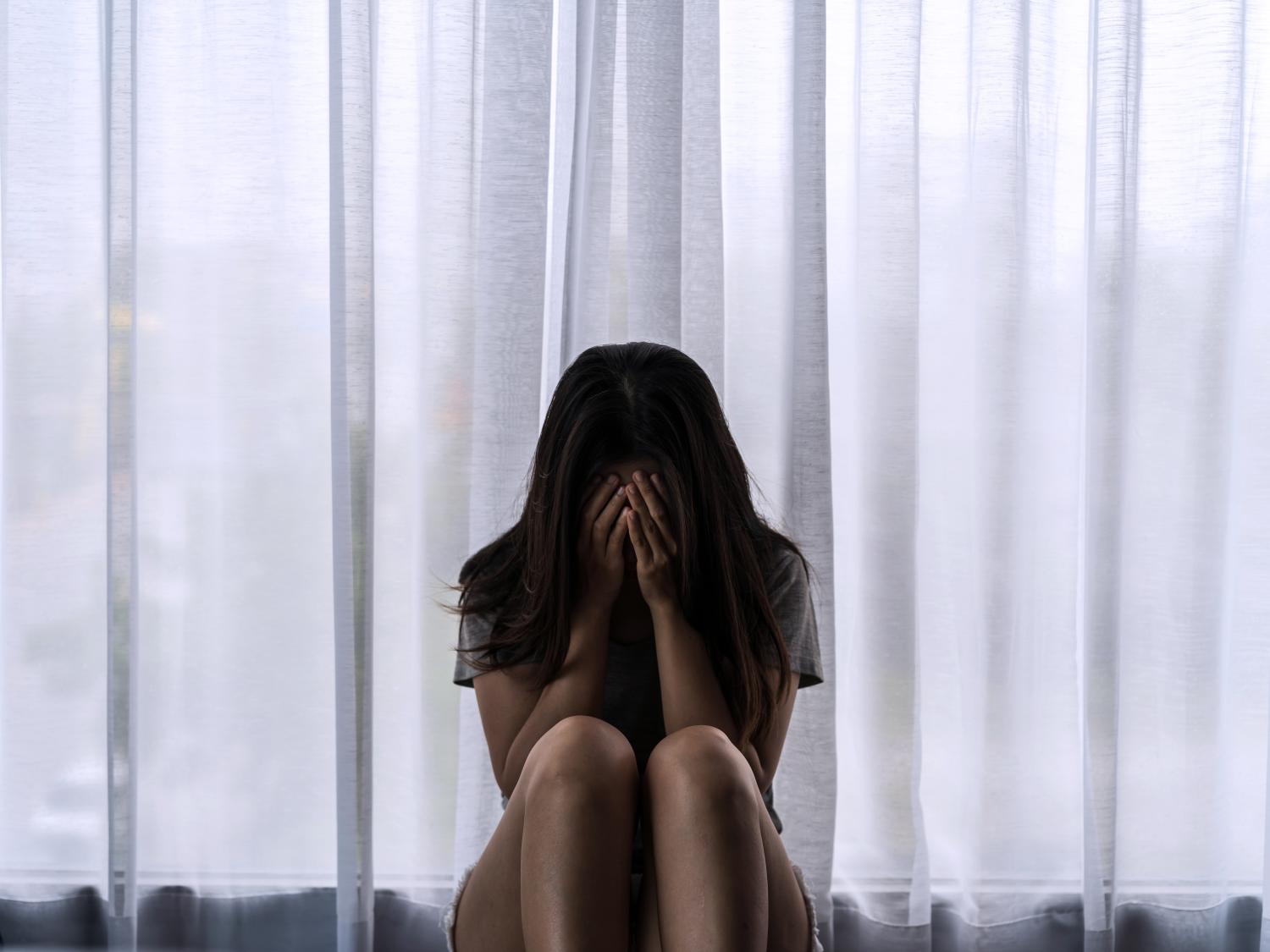 A woman sitting in front of a window with her face in her hands.