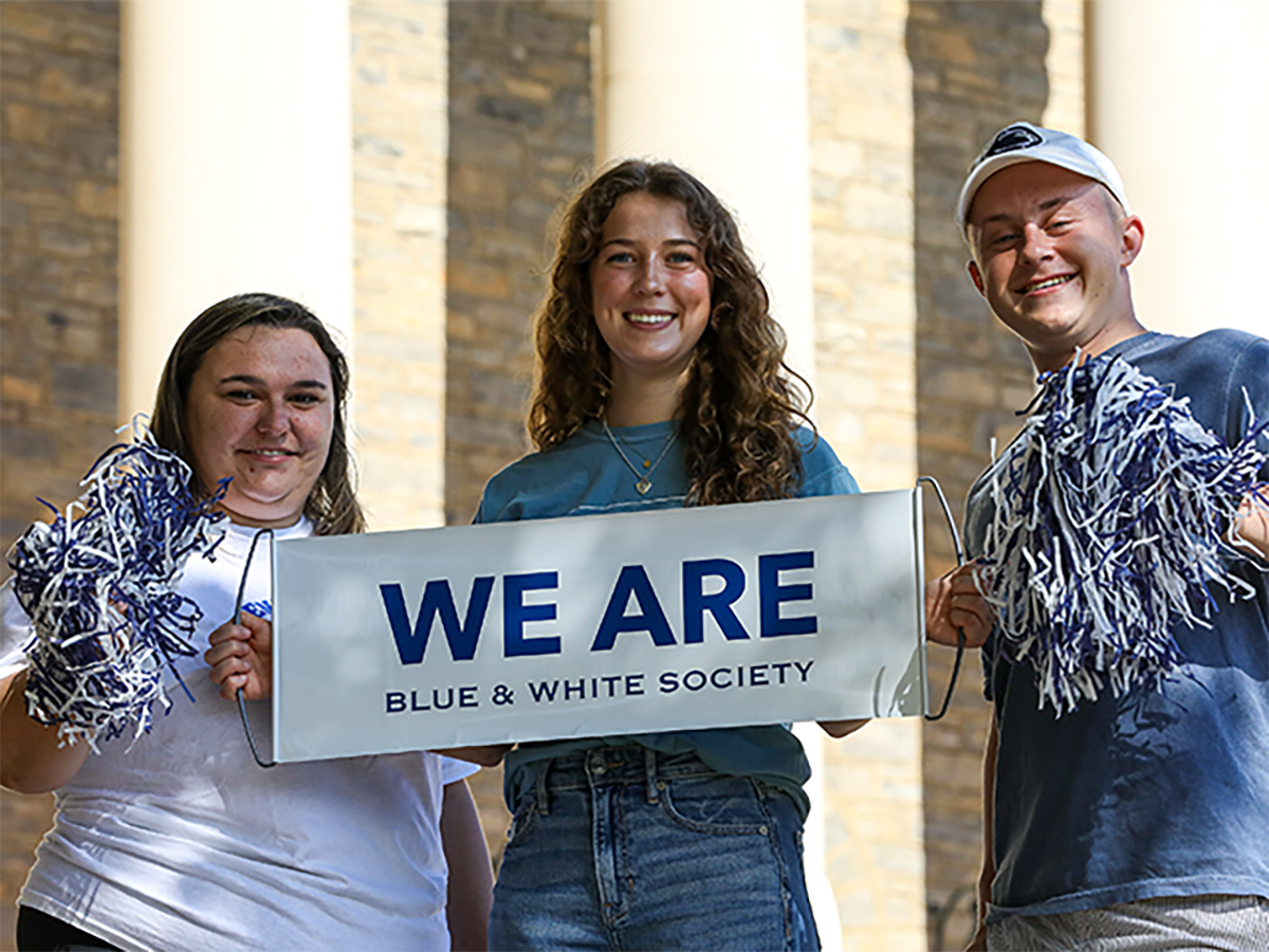 Three individuals standing with a sign that says "We Are Blue & White society"
