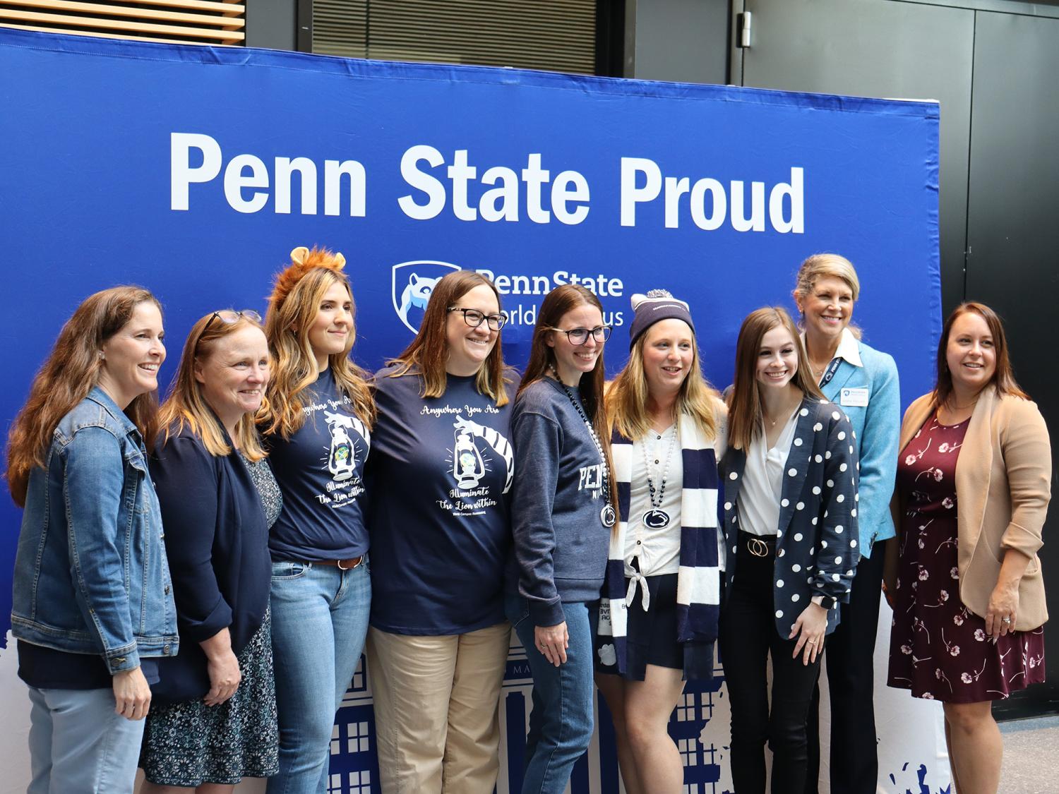 A group of people pose for a photo in front of a Penn State background.