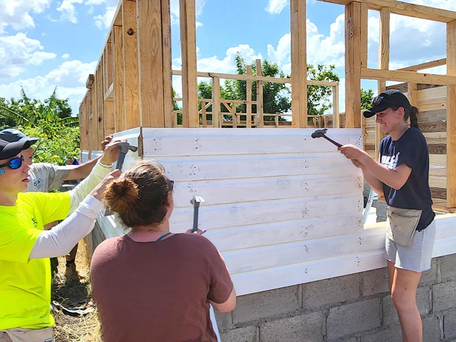 Three students work on putting siding on a familiy home