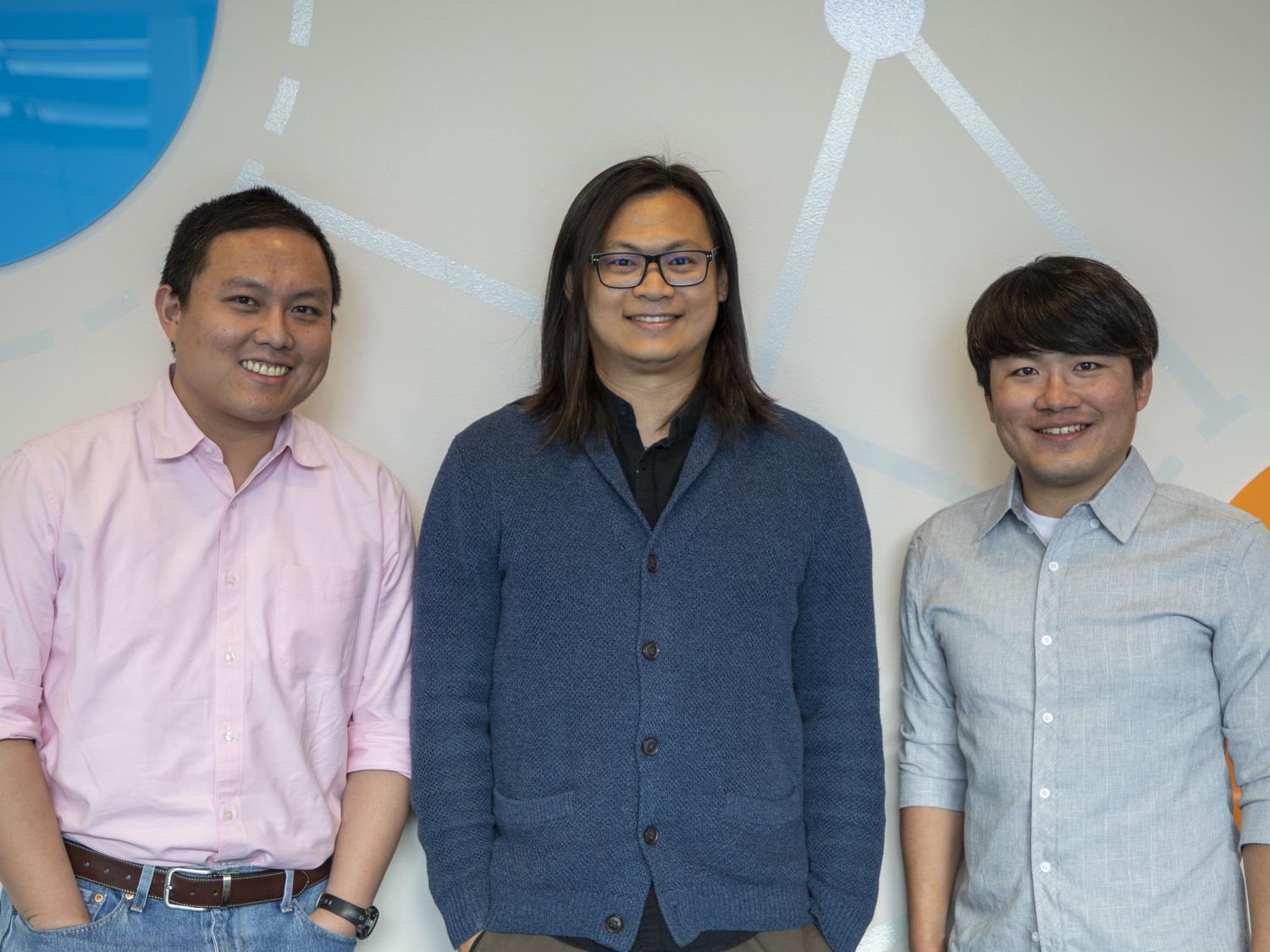 Three smiling people standing against a colorful wall