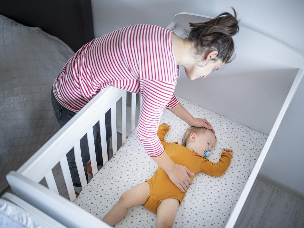 A mother puts her baby to sleep in a crib.