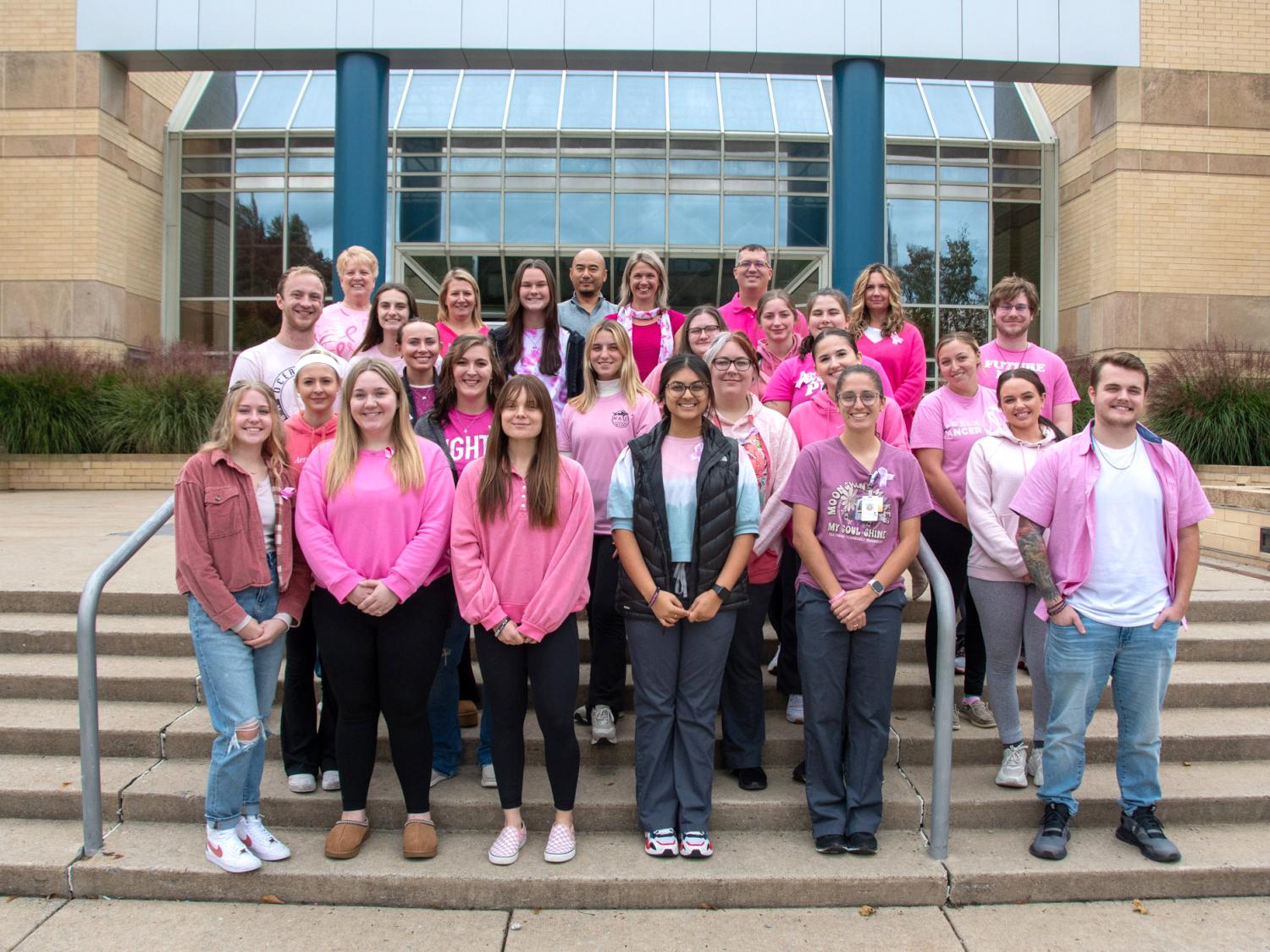 A group of people wearing pink tee shirts pose for a photo on the steps of a building
