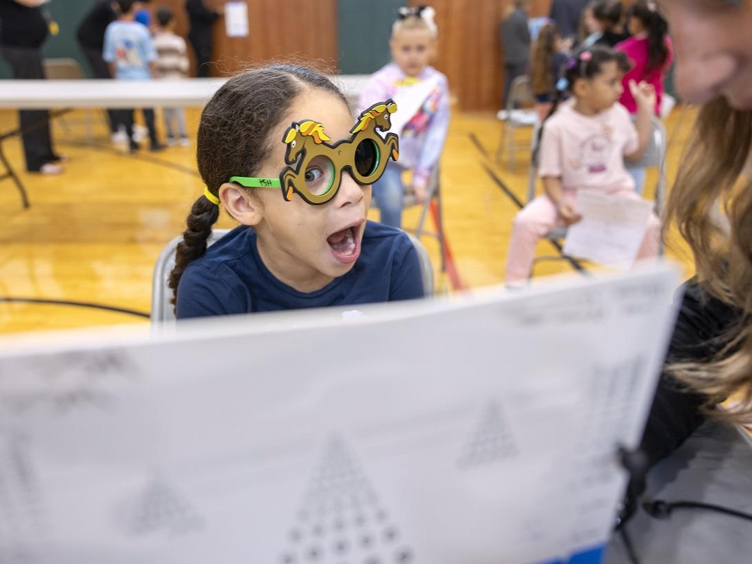 A little girl in pigtails makes a face behind glasses at a form.