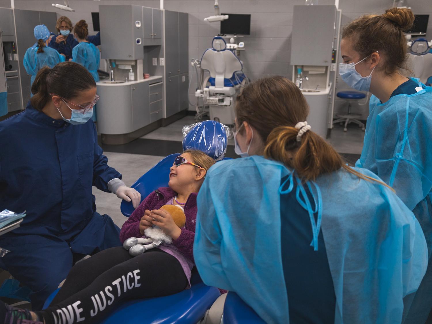 An adult and group of dental hygiene students provide dental healthcare to a child