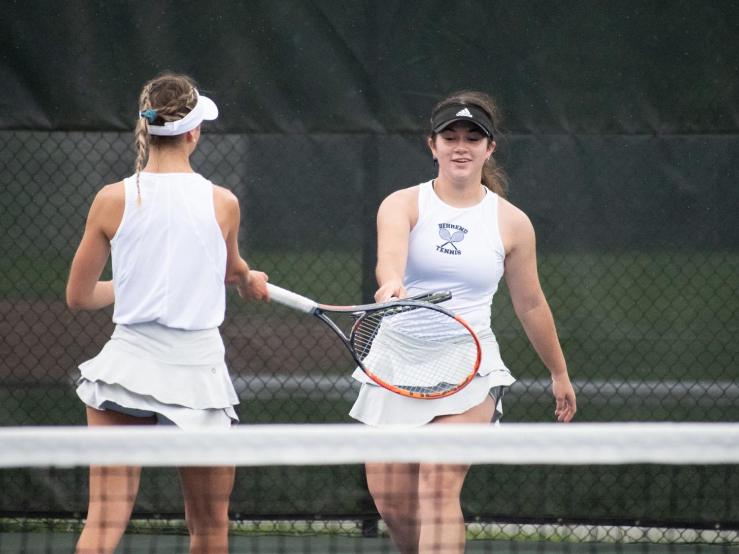 Two Penn State Behrend tennis players touch rackets after scoring a point.