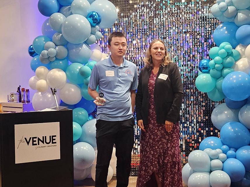 A man holding an award and a woman next to him standing on stage near a podium