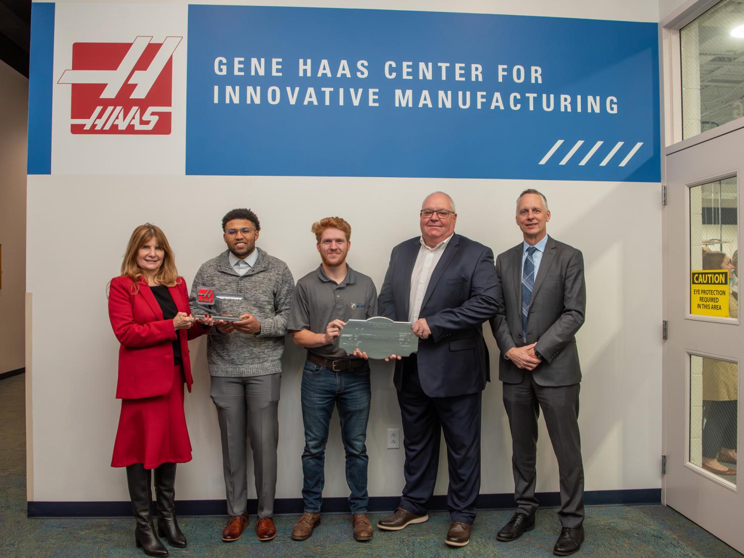 Five people pose for a photograph at a dedication ceremony standing under a sign that reads Gene Haas Center for Innovative Manufacturing