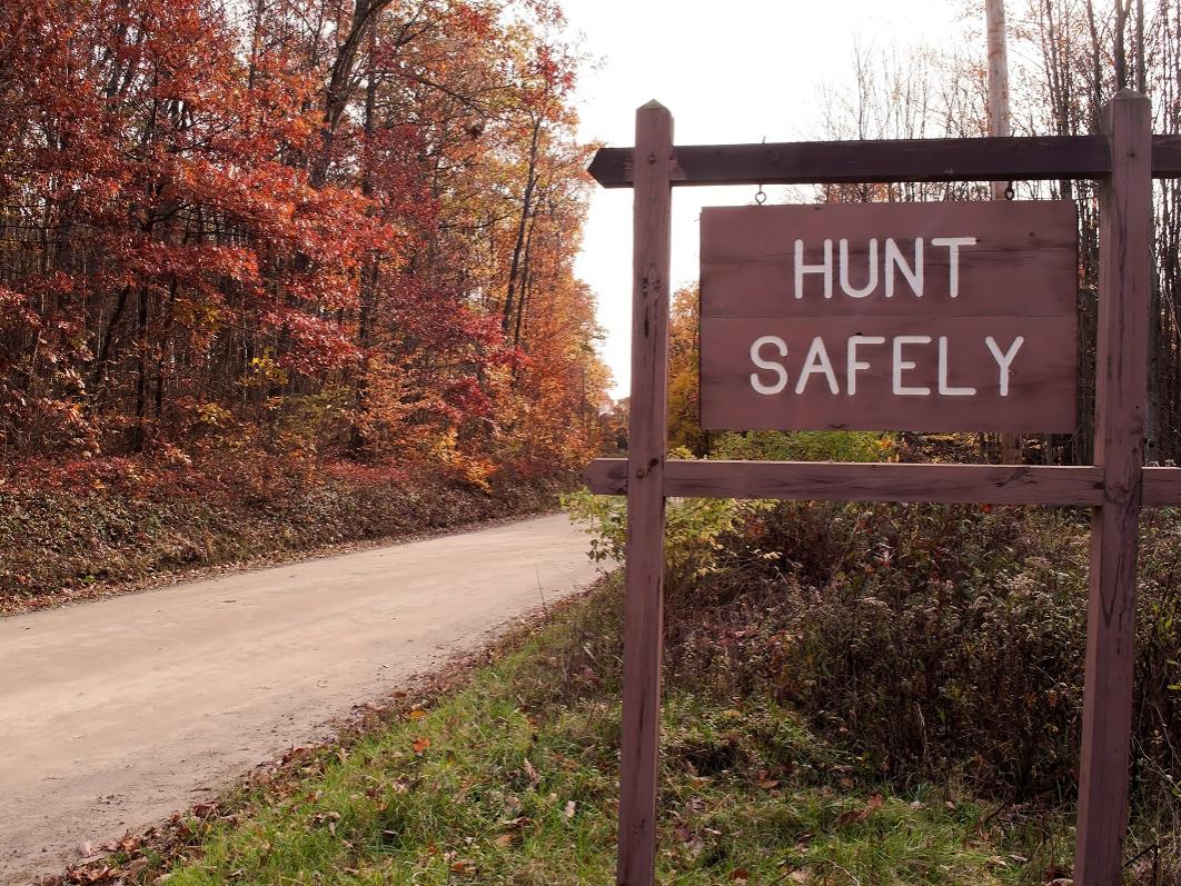 A "hunt safely" sign on the side of a dirt road in the fall woods.