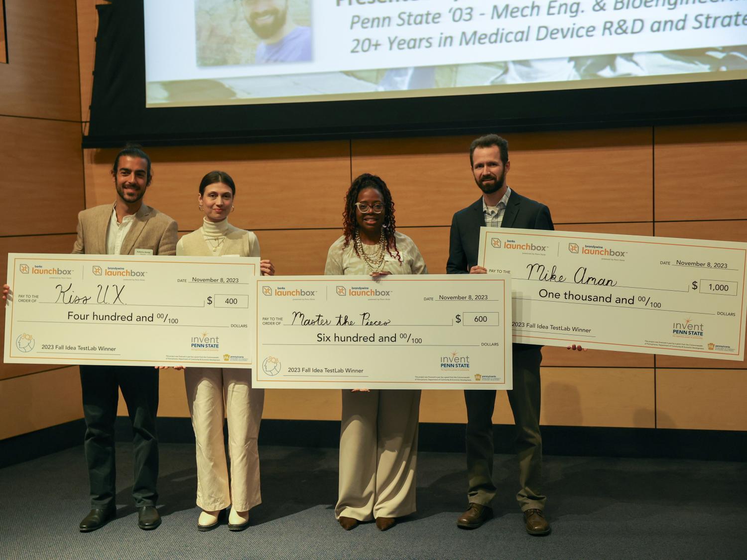 winners of idea TestLab competition standing on stage with large checks for $400, $600 and $1000