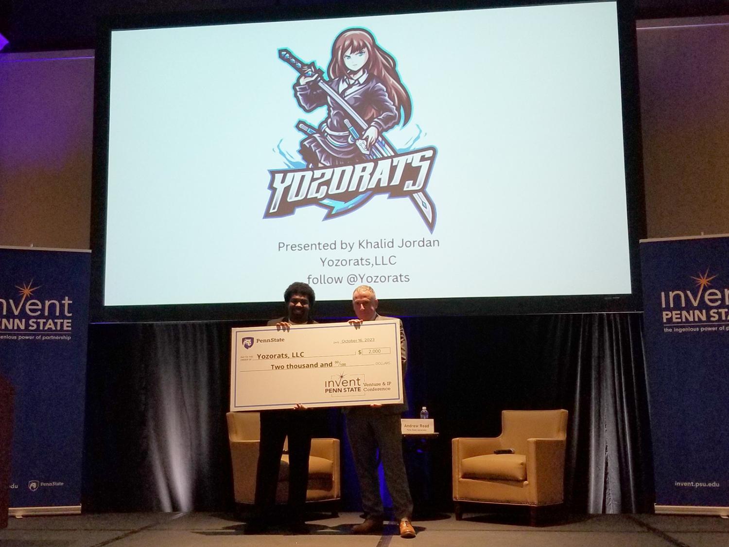 Khalid Jordan holding large check for $2000 with Invent Penn State representative