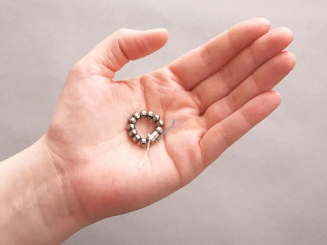 A hand holding the LINX device, a small band of magnetic titanium beads