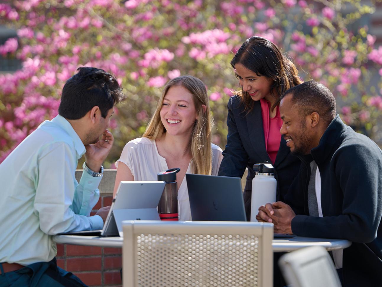A photo of four students, two male, two female sitting outside with laptops and water bottles.