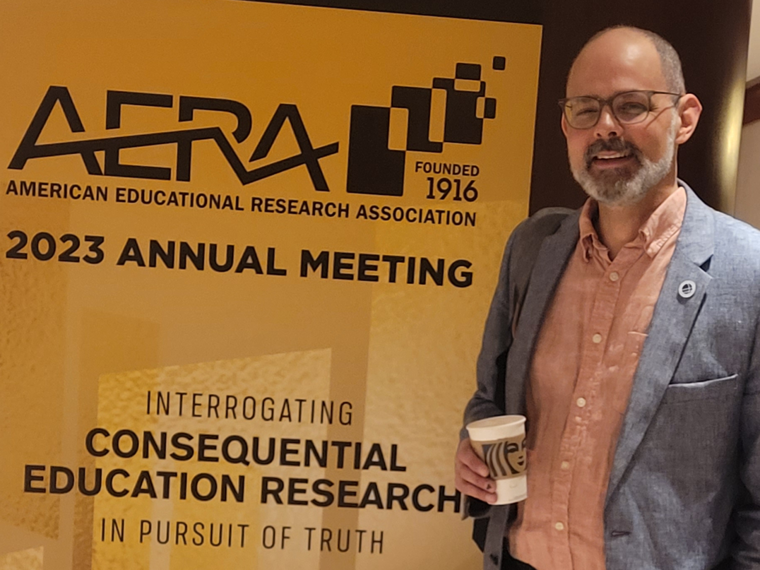 Joseph Polizzi stands in front of a sign at the 2023 AERA conference in Chicago.