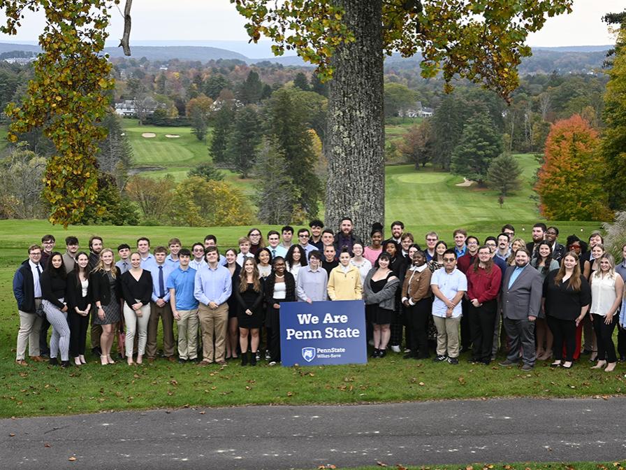 A large group of students standing outdoors with a sign that says We Are Penn State
